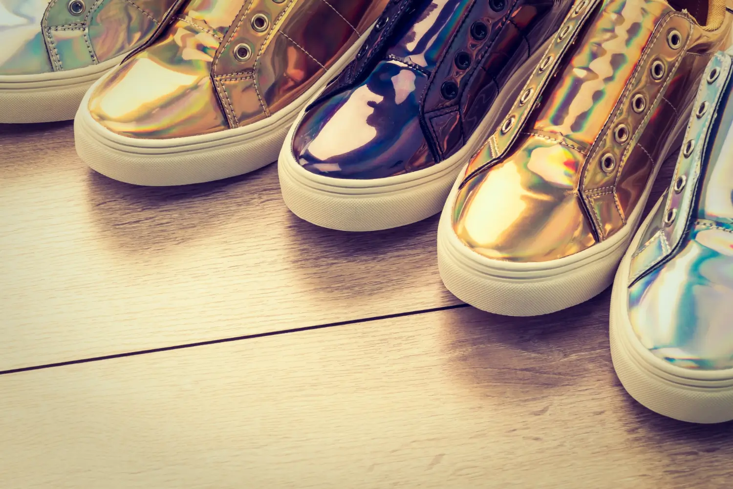 Zapatillas brillantes de diferentes colores en un fondo de madera clara, destacando su diseño moderno y estilo llamativo.