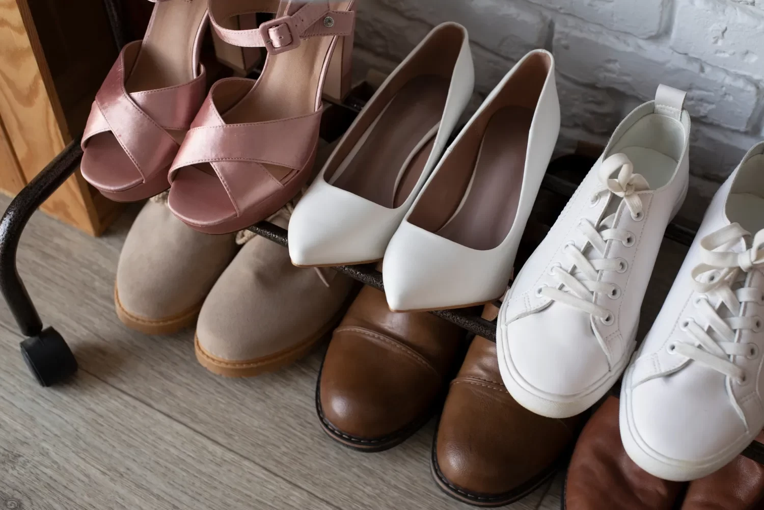 Colección de zapatos en estante, incluyendo sandalias rosas, tacones blancos, botas de gamuza, zapatos marrones y zapatillas blancas. Ideal para mostrar variedad de estilos de calzado.